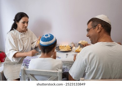  jewish family celebrating hanukkah, israel, boy in kippah, jewish holidays, yom kippur feast, table with food, honey, donuts, family holiday, religious family, family praying, Jewish woman - Powered by Shutterstock