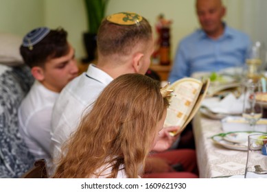 Jewish Family Celebrating Passover Seder Reading The Haggadah. Three Generations, Real Family.