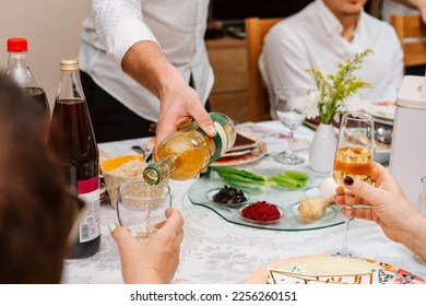 Jewish family celebrating Passover at the table with traditional food. Family Passover dinner seder. Young man pouring wine in the glass and boy reading haggadah, woman raises a wine glas - Powered by Shutterstock