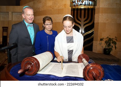 A Jewish Girl in the temple for her Bat Mitzvah. She is holding a yad in front of the Torah