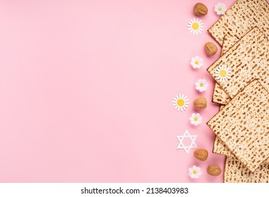 Jewish holiday Passover greeting card concept with matzah, nuts, tulip and daisy flowers on pink table. Seder Pesach spring holiday background, top view, copy space.