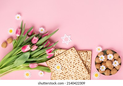 Jewish Holiday Passover Greeting Card Concept With Matzah, Nuts, Tulip And Daisy Flowers On Pink Table. Seder Pesach Spring Holiday Background, Top View, Copy Space.