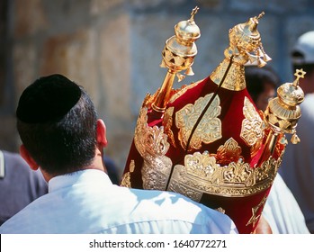 Еврей в черной кипе со свитком Торы в красном футляре с золотыми колокольчиками и коронами (риммонимом) и другими украшениями - Симхат Тора; Западная стена, Иерусалим