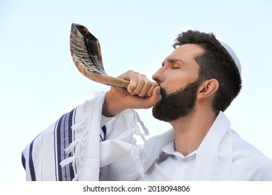 Jewish Man In Kippah And Tallit Blowing Shofar Outdoors. Rosh Hashanah Celebration