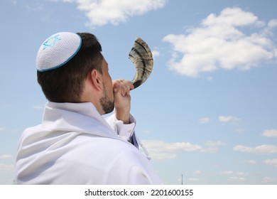 Jewish Man In Kippah And Tallit Blowing Shofar Outdoors. Rosh Hashanah Celebration