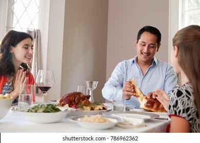 Jewish man sharing challah bread with family at Shabbat meal