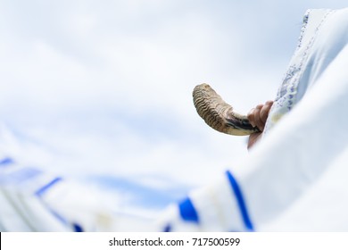 Jewish man in Tallit blowing the Shofar (horn) of Rosh Hashanah (New Year Jew) on sunset sky.Religious and Holidays symbol concept.