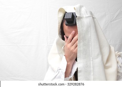 Jewish Man wrapped in tefillin And Talit And pray.
A religious orthodox Jew with arm-tefillin on his left hand prays