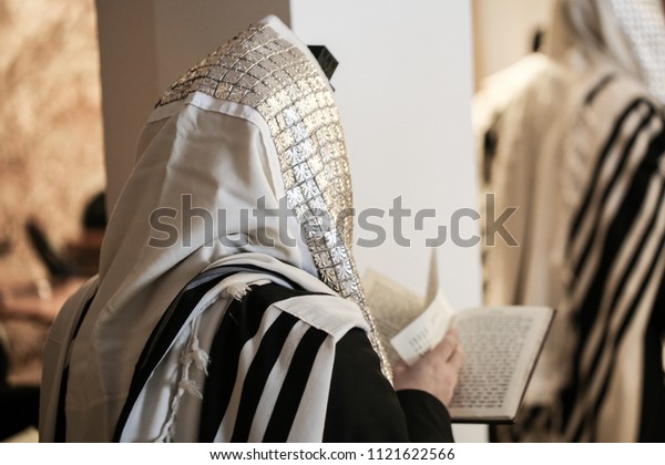 Jewish orthodox man wrapped in prayer shawl from a\
side view
