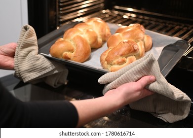 Jewish woman taking out baked Challah Bread from the oven before Sabbath Jewish Holiday.
