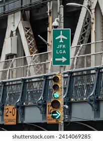 JFK and LGA sign on traffic light with manhattan bridge in the background (close up of directional signs to john f kennedy, laguardia airport) green light signal