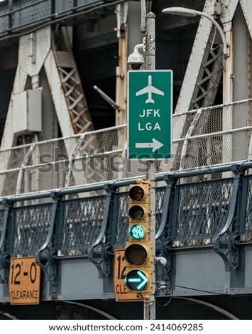 JFK and LGA sign on traffic light with manhattan bridge in the background (close up of directional signs to john f kennedy, laguardia airport) green light signal