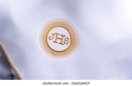 JHS Christian symbol on a communion child. JHS Christogram embroidered with gold thread on a white alba. First Holy Communion dress.