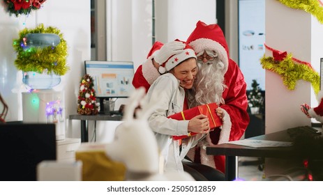 Jib up revealing shot of worker receiving gifts from colleague dressed as Santa Claus in xmas adorn workplace. Disguised coworker surprising woman with presents before office Secret Santa party - Powered by Shutterstock