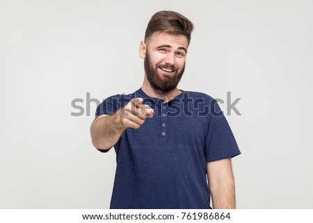 Jibe, bad taunt concept. Young adult man pointing finger and toothy smile. Studio shot, gray background