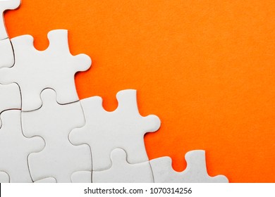 Jigsaw puzzle pieces and business concept with a border made of puzzle pieces on colorful bright orange background with copy space