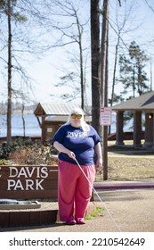 JIMMIE DAVIS STATE PARK, LOUISIANA, UNITED STATES - MARCH 18 2022: Blind Woman With A Cane Standing In Front Of The Jimmie Davis State Park Sign