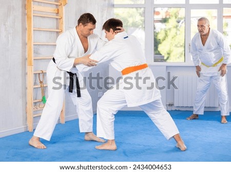 Jiu-jitsu master demonstrating basic martial art grabs and throws during sparring with young novice fighter at training..