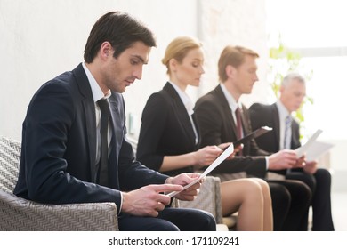 Job candidates. Four people in formalwear waiting in line while sitting at the chairs and holding papers in their hands - Powered by Shutterstock