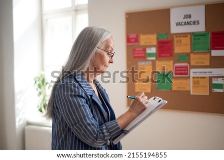 Job center employee with file form standing in front of employment noticeboard.