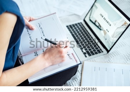 Job interview, Finding New Job. Young woman writing in Planner diary notes about job interview sitting near laptop on the bed at home
