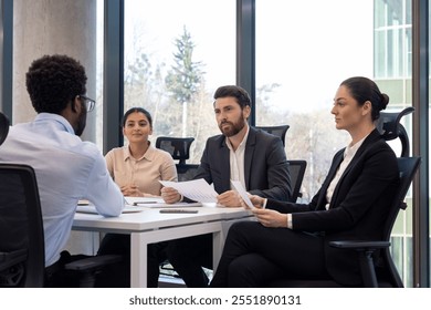 Job interview scene with diverse business team and candidate engaging professionally in modern office setting. Panel holding documents, tables equipped for corporate discussions. - Powered by Shutterstock