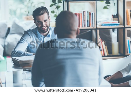 Job interview. Two young men in smart casual wear sitting at the office desk together while one of them smiling 