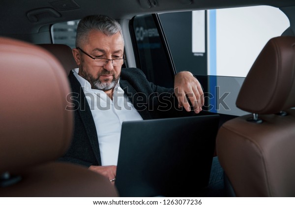 Job out of the office.\
Working on a back of car using silver colored laptop. Senior\
businessman.