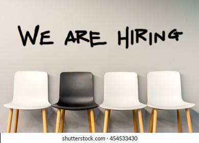 Job recruiting advertisement represented by 'WE ARE HIRING' texts on the chairs or wall. One chair is colored differently to represent the hiring position to be recruited and filled.