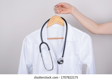 Job vacancy concept. Cropped close up photo of hand holding white doctor coat on hanger isolated over grey background