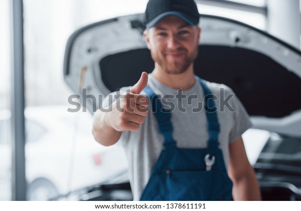 Job well done. Employee in the blue\
colored uniform stands in the automobile\
salon.