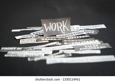 Jobs Or Careers Concept: Multiple Job Titles Or Occupations Cut Off From Newspaper With Work On Top Of The Pile And On Black Background