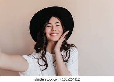 Jocund Asian Girl In Hat Laughing At Camera. Glamorous Chinese Woman Taking Selfie.