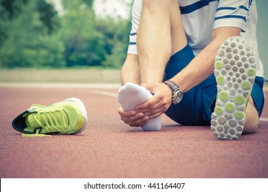 Jogger Hands On Foot. He Is Feeling Pain As His Ankle Or Foot Is Broken Or Twisted. Accident On Running Track During The Morning Exercise. Sport Accident And Foot Sprain Concepts.