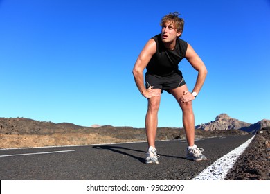 Jogger resting after running. Man runner taking a break during training outdoors in amazing landscape. Young Caucasian male fitness model after work out.