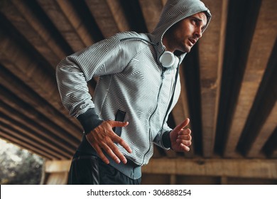 Jogger running in city environment.He wearing headphones around neck.