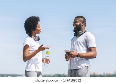 Jogging Coaching Concept. Happy Black Couple Talking About Morning Running Training Plan Near River Bank In City.