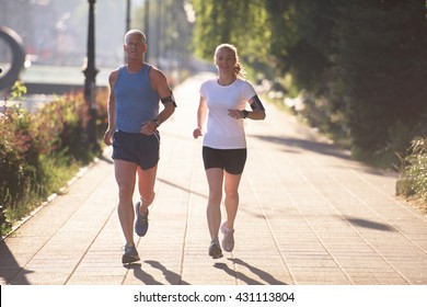 Jogging Couple Warming Up And Stretching Before Morning Running Training Workout  In The City With Sunrise In Background