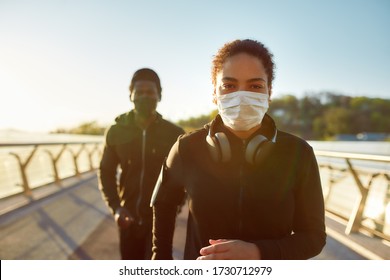 Jogging During Quarantine. Young African Couple Wearing Face Medical Masks While Running Together On The Bridge In The Morning. Sport And Coronavirus. Covid-19. Protection. Social Distancing