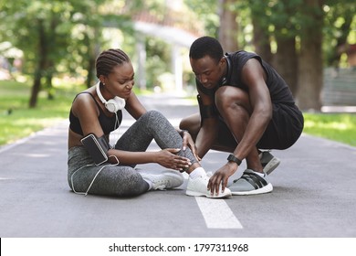 Jogging Injuries. Caring Black Guy Helping Girlfriend Suffering From Sprained Ankle Trauma During Running In Park, Free Space