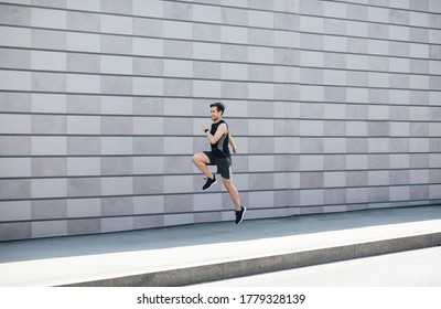 Jogging with jumping. Guy runs at path near gray brick wall in city in daylight, free space