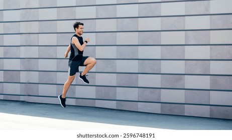 Jogging with jumping. Guy runs at path near gray brick wall in city in daylight, free space