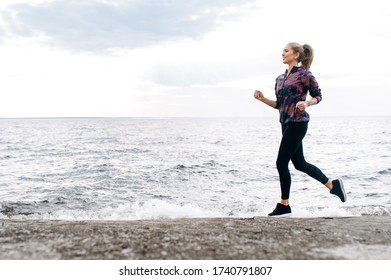 Jogging outdoors. Cardio workout. Young attractive athletic girl in sportswear is jogging outdoor near the sea - Shutterstock ID 1740791807