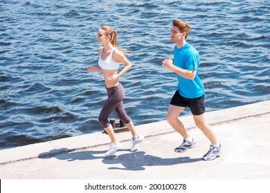 Jogging Together.  Top View Of Young Woman And Man In Sports Clothing Running Along The Riverbank  