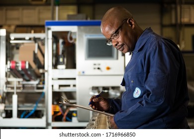 Johannesburg, South Africa - August 13, 2015:  African Male Supervisor Checking A Clipboard On A Packaging Plant Assembly Line