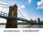 The John A. Roebling Suspension Bridge and Cincinnati skyline shot from Kentucky side. Partly cloudy blue skies.