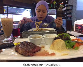 JOHOR BAHRU,JOHOR-APRIL 20 219:A Hijab Malay Woman Eats A Plate Of Carbonara With A Plate Of Beef Steal Serve To Her Partner At Me’Nate Cafe In Johor Bahru