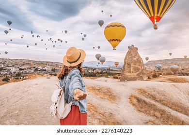 Join the adventure in Cappadocia, Turkey as a young woman strikes a confident follow me pose with hot air balloons soaring in the background.