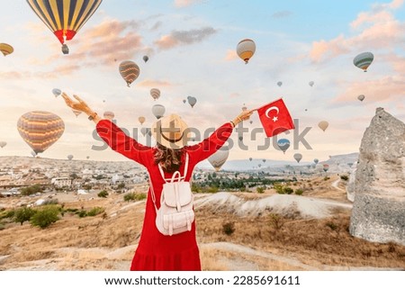 Join a young woman as she watches the iconic hot air balloons of Cappadocia, Turkey while proudly displaying the Turkish flag. A celebration of the country's beauty and culture.