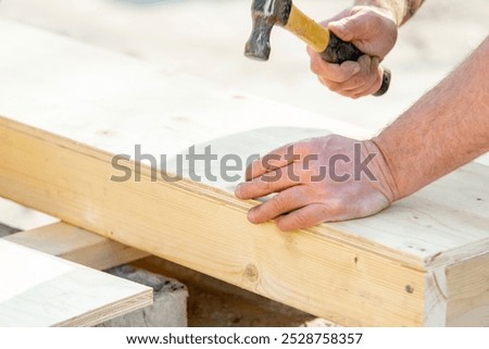 Joiner carpenter assembling formwork shutter. Crafting a wooden structure with precise hammer strikes at a sunny outdoor workshop in the afternoon